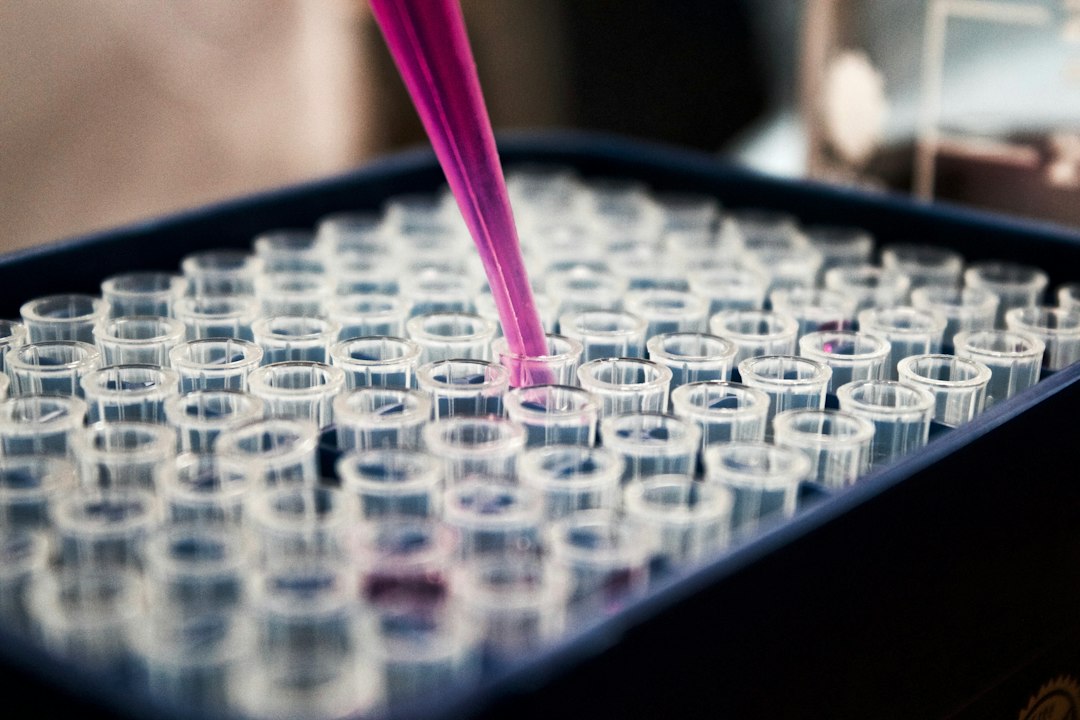 Close-up of a pipette dispensing liquid into small test tubes in a laboratory setting.